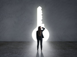 Find a solution and way concept with back of pensive businesswoman grabbing her head in black suit looking at big bright and glowing keyhole in grey wall